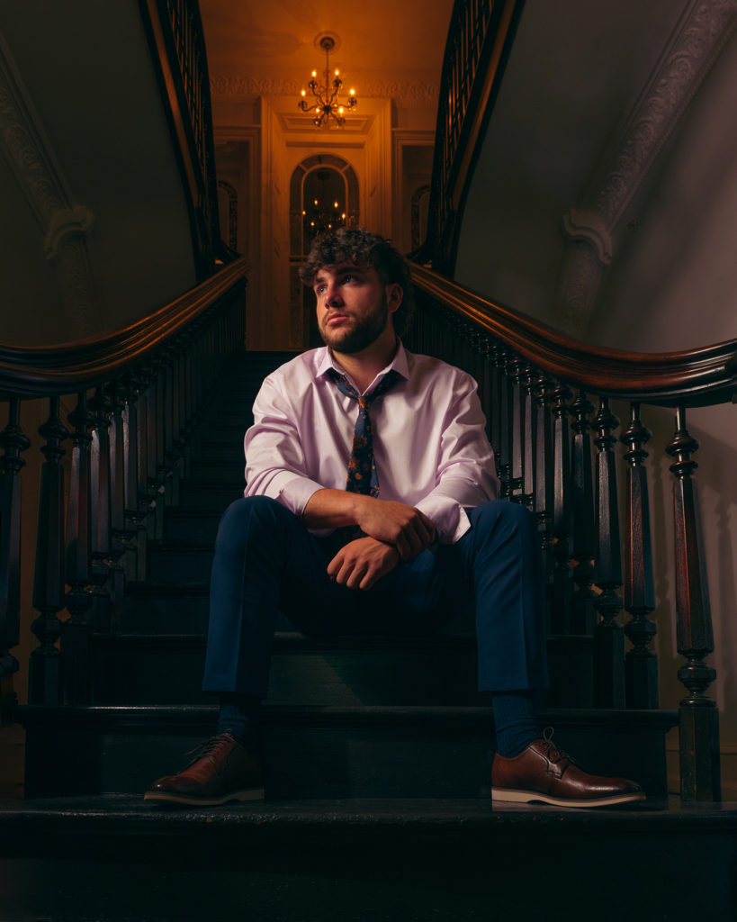 Teen male in shirt and tie sitting on darkened steps.