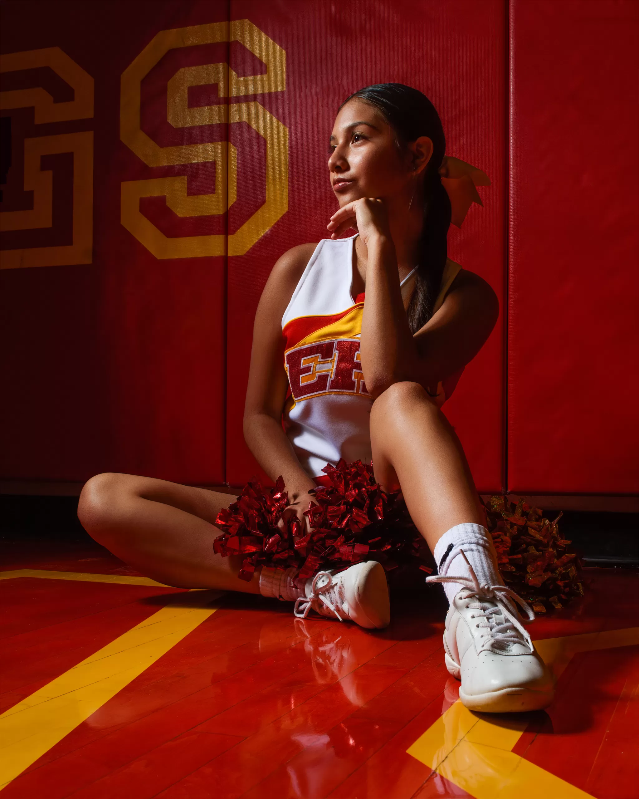 Cheerleader in the gym sitting on the floor.