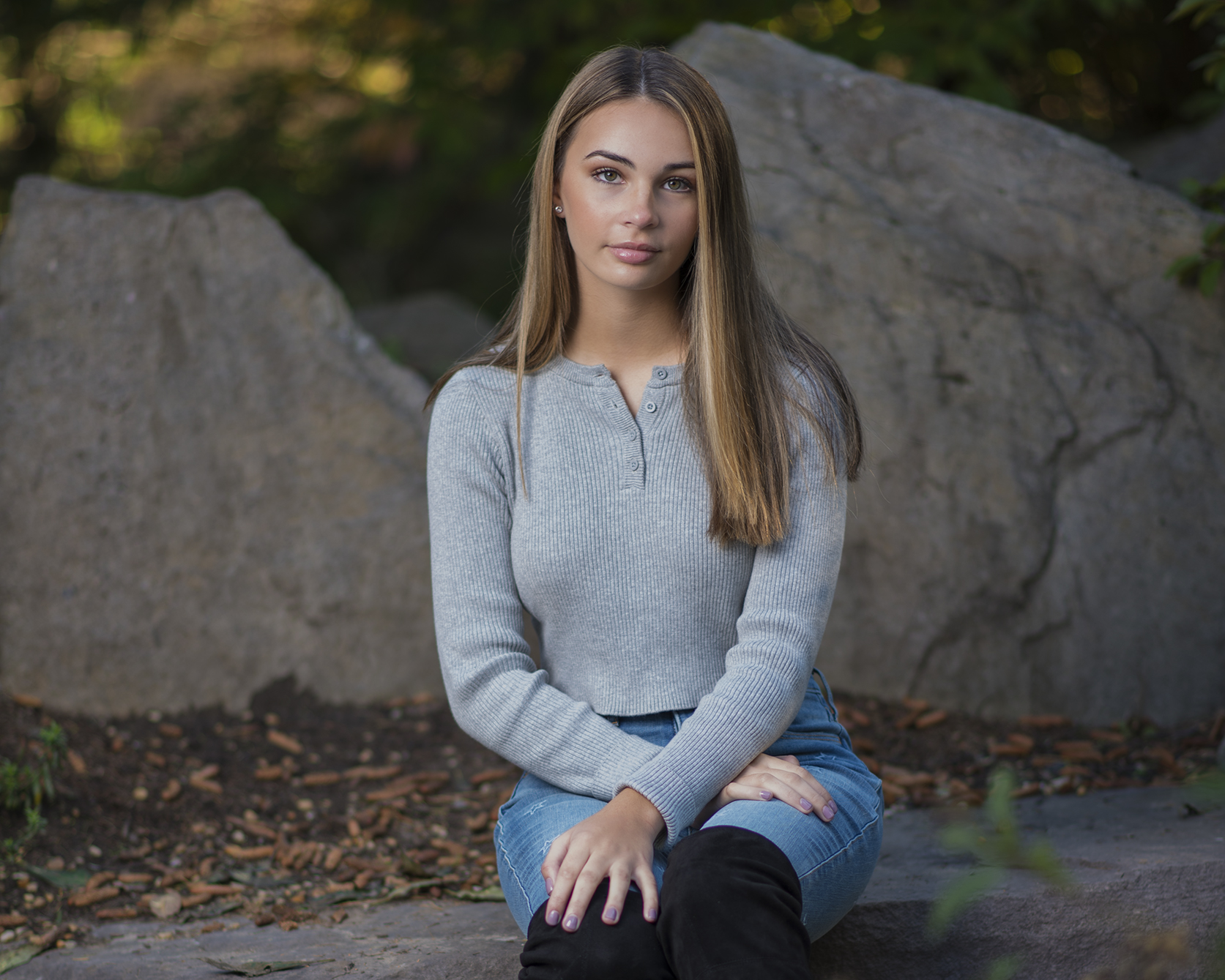 Girl sitting on a rock in a wooded area.