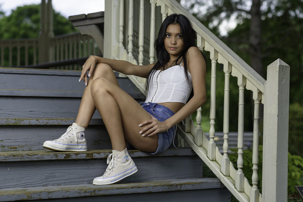 Girl with jean shorts and white top sitting on pavilion steps.